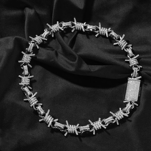 Macro detail of iced-out barbed wire necklace with pavé zircons on black silk backdrop