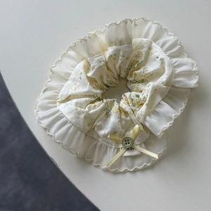 Detailed close-up of floral scrunchie with yellow bow and button on beige cotton fabric