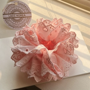 Détail d'un chouchou en dentelle rose clair avec broderie ajourée et bords festonnés