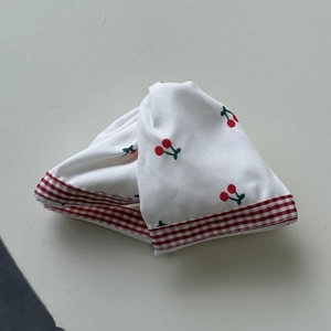 Detail of soft white cotton hair tie featuring red cherry patterns and lace edges