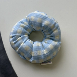 Close-up detail of light blue checkered fabric scrunchie with soft cotton texture and tag