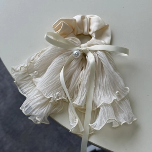 Détail d'un chouchou élégant en satin beige avec mousseline plissée et perles blanches