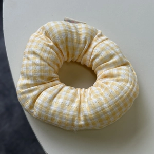 Close-up of yellow gingham scrunchie with soft fabric texture and decorative brand tag