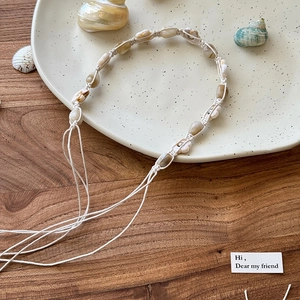 Détail d'un collier de coquillages bohème tressé main avec pompons réglables sur un plateau