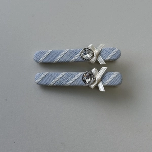 Détail de pinces à cheveux en tissu rayé bleu clair avec nœuds blancs et strass brillants