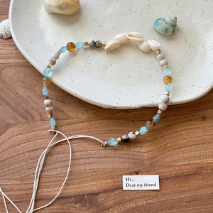 Détail d'un bandeau bohème tressé avec coquillages et perles colorées sur plateau blanc
