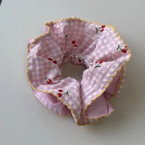 Detailed shot of pink gingham scrunchie with cherry print and yellow wavy stitching
