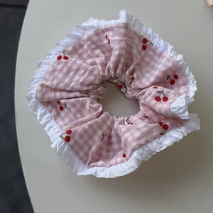 Detailed close-up of pink checkered scrunchie with cherry print and white lace edges
