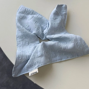 Gros plan du chouchou en dentelle bleu clair avec texture florale et étiquette