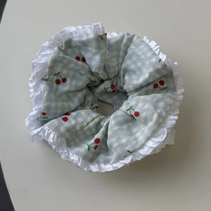 Detailed shot of light blue gingham scrunchie with cherry print and white lace trim