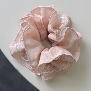 Détail du chouchou en mousseline rose avec broderie délicate de dentelle blanche