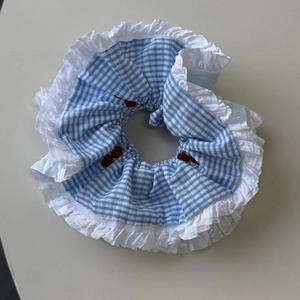 Close-up of blue gingham hair scrunchie with white lace trim and red cherry embroidery