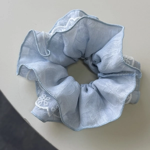 Détail d'un chouchou bleu clair avec broderie florale blanche et plis élégants