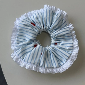 Detail of blue striped hair scrunchie with white lace trim and red heart embroidery