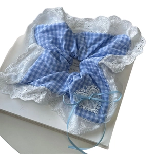 Blue gingham scrunchie with white lace trim and a heart-shaped bow detail on a book