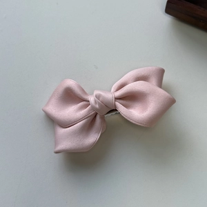 Detail shot of a light pink satin double-layered bow hair clip on a clean ivory surface