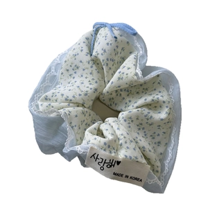 Haarscrunchie met bloemenprint, delicate kanten rand en blauw lint op een witte achtergrond
