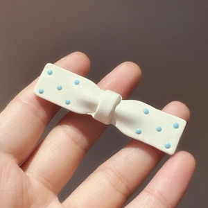 Detail of cute cream white bow hair clip with blue polka dots held by hand