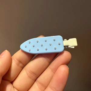 Detailed close-up of light blue polka dot hair clip with white pearls and metal alligator clip