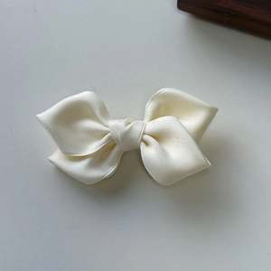 Detail of off-white satin bow hair clip featuring premium twill texture and double-layered design