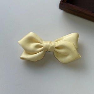 Detail of a pale yellow satin bow hair clip with smooth ribbon texture and center knot