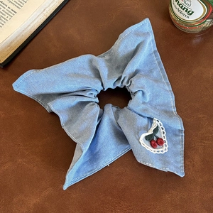 Close-up of blue denim scrunchie with lace heart patch and cherry embroidery detail
