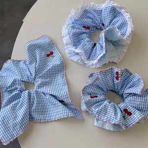 Close-up of blue gingham cherry embroidered hair scrunchies with white lace and bow