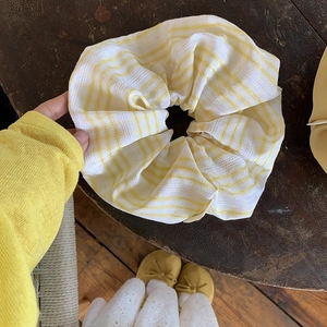 Detail eines großen gelben Karo-Scrunchies mit Spitzenkanten auf Holzuntergrund