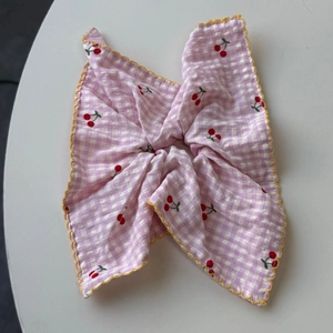Detail of pink plaid scrunchie with red cherry prints and yellow wavy scalloped edges