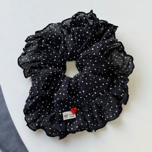 Détail d'un chouchou noir à pois avec un bouton coeur rouge et une étiquette faite à la main