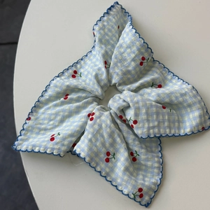 Close-up of blue plaid scrunchie with red cherry prints and scalloped embroidery edges