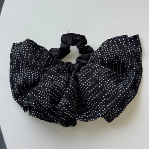 Detail of a black and white polka dot scrunchie with soft chiffon pleats and ruffled texture