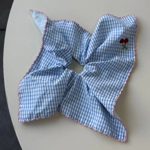 Detailed view of blue gingham hair scrunchie with pink scalloped edges and cherry embroidery