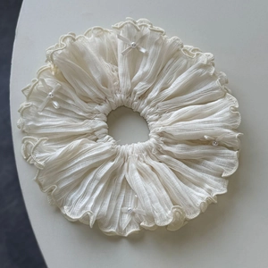 Detailed macro view of white pleated fabric scrunchie with pearl bow accents