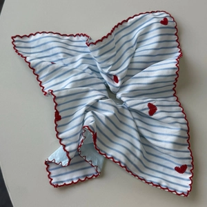Detail of blue striped fabric with red scalloped edges and embroidered red hearts