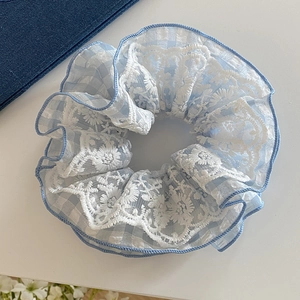 Close-up of light blue plaid scrunchie with white lace floral embroidery and ruffled edge