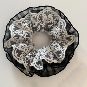 Detail view of plaid fabric scrunchie with layered floral lace embroidery and soft texture