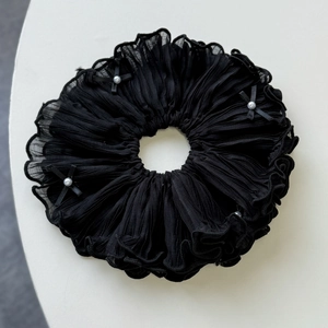 Detailed close-up of a pleated black scrunchie with elegant pearls and small ribbon bows