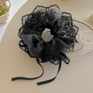 Détail d'un chouchou en dentelle noire avec broderie florale et rubans de satin pendants