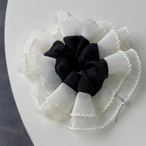 Detailed shot of black satin hair scrunchie with white pleated lace trim on white background