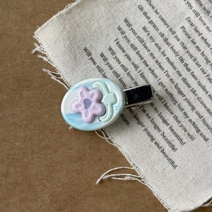 Close-up of a blue acetate oval hair clip featuring a purple flower on vintage fabric