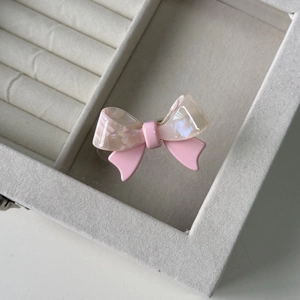 Detailed close-up of bow hair clip with marble texture acetate and pink finish