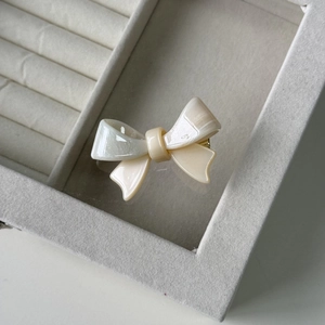 Detail view of a glossy ivory bow hair clip with pearlescent texture on a jewelry box