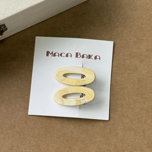 Détail de barrettes ovales en acétate avec motif marbré crème sur carte de présentation