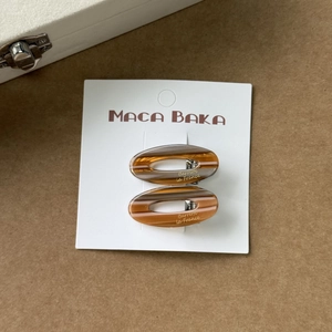 Détail de deux barrettes ovales évidées en acétate ambré sur une carte d'exposition