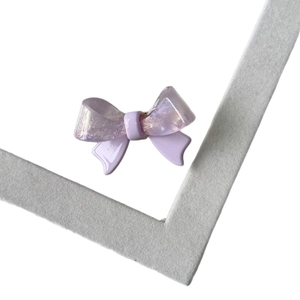 Sparkly purple acetate bow hair clip with glitter finish on a grey display stand