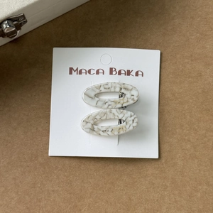 Gros plan d'un lot de deux barrettes ovales en acétate blanc à texture marbrée sur carte