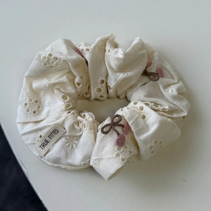 Détail de la broderie florale sur chouchou crème avec accents de cerises roses 3D