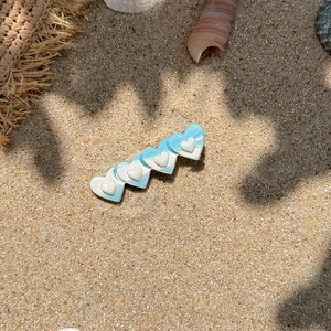 Close-up of beach style hair clip with blue and white gradient hearts on sand