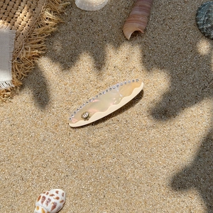 Detail of seashell heart hair clip with pearls and rhinestones on sandy beach scene